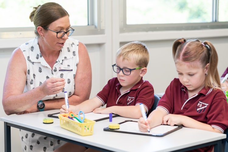 Picture of teacher engaging in lesson with 2 students writting on white boards