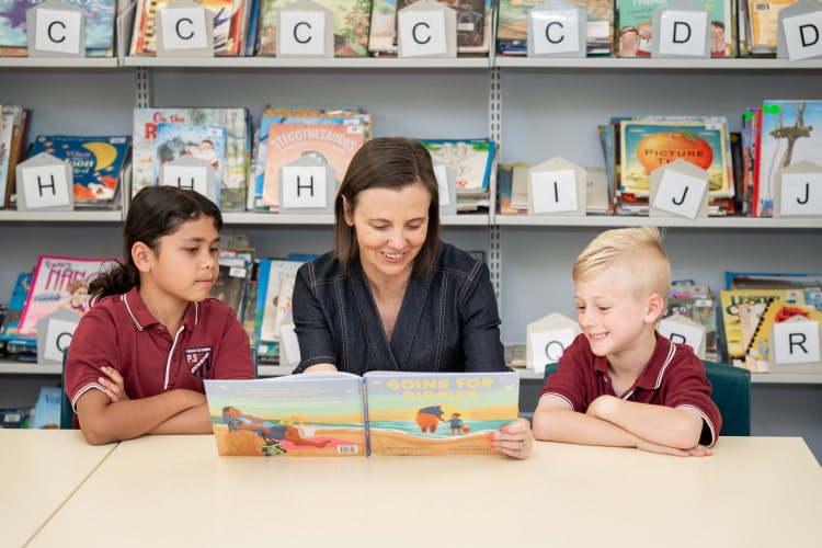 Picture of teacher reading to 2 students in library