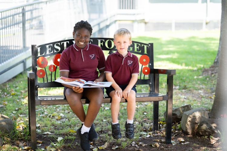 2 students smiling reading a book on the school anzac chair