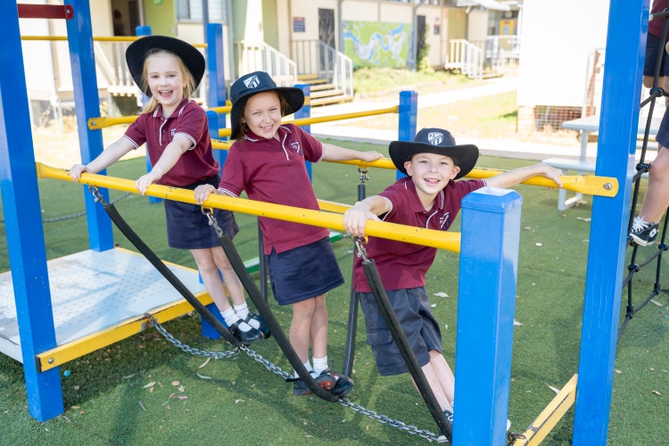 3 students on play equipment smiling