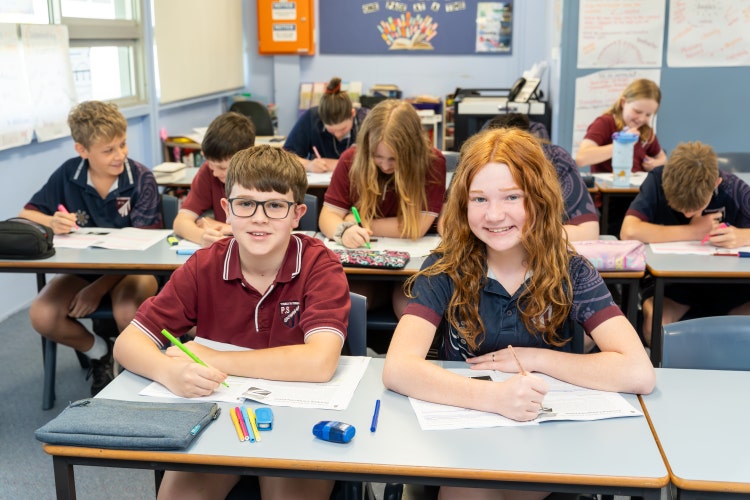 picture of 2 students learning and writing in books in classroom